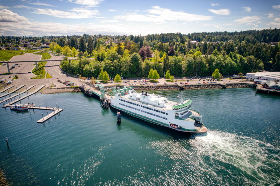a large ferry departs a dock near point defiance with a park and trees behind