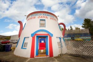 a photo of the world famous bob's java jive on a sunny day. A white building shaped like a teapot with red handle, spout, and front door.