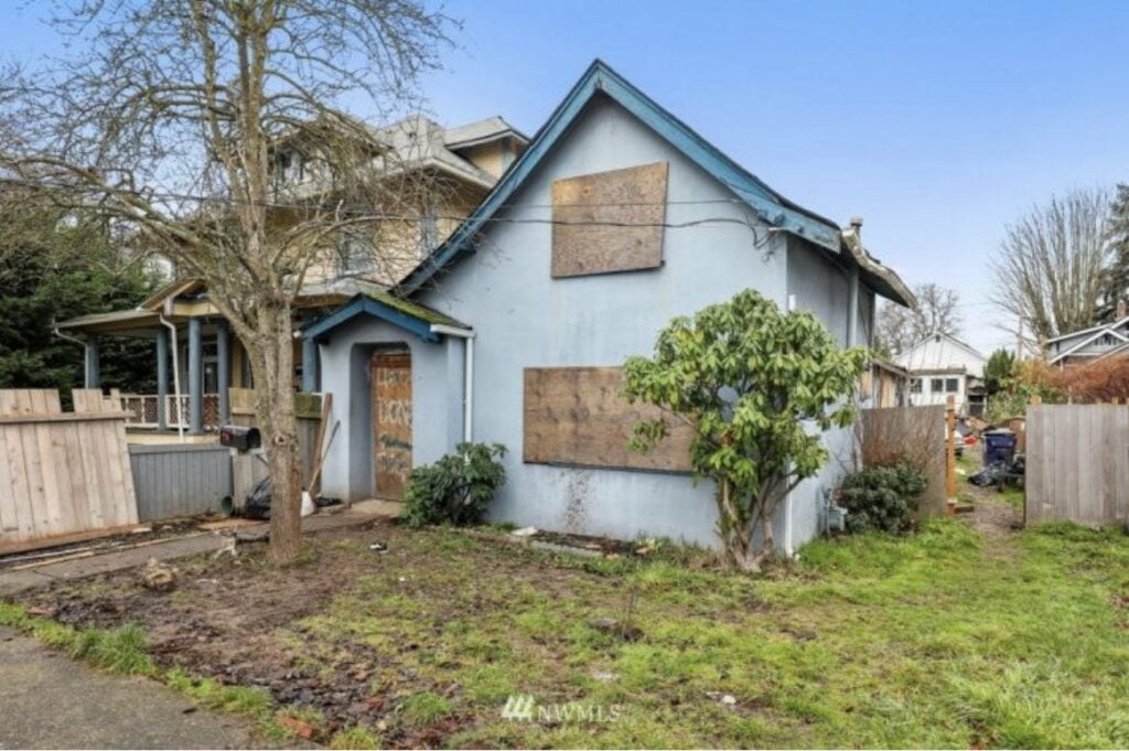 photo of a pale blue house with dark blue trim with boarded up windows and doors in tacoma wa