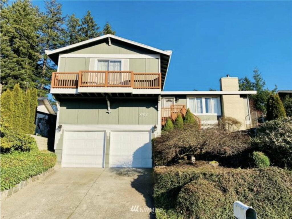 a green two story house at the top of a driveway with white garage doors in the wapato neighborhood of tacoma