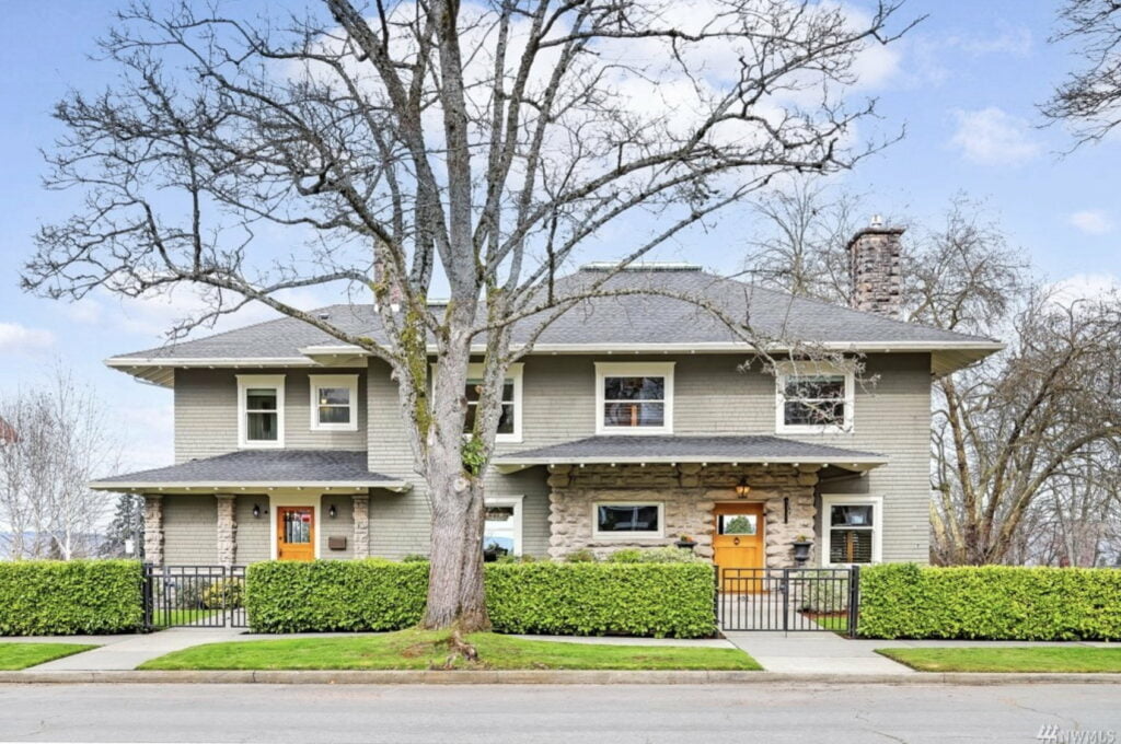 a photo of a large beige house with orange doors with a tree with no leaves in front of it on Tacomas north yakima avenue