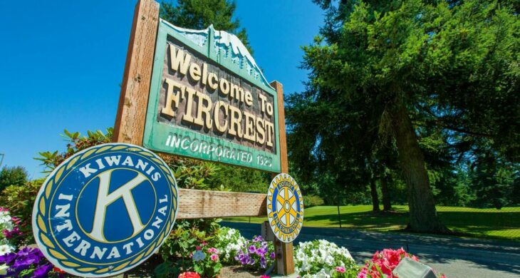 A photo of a green sign saying welcome to fircrest incorporated 1925 with flowers growing around it