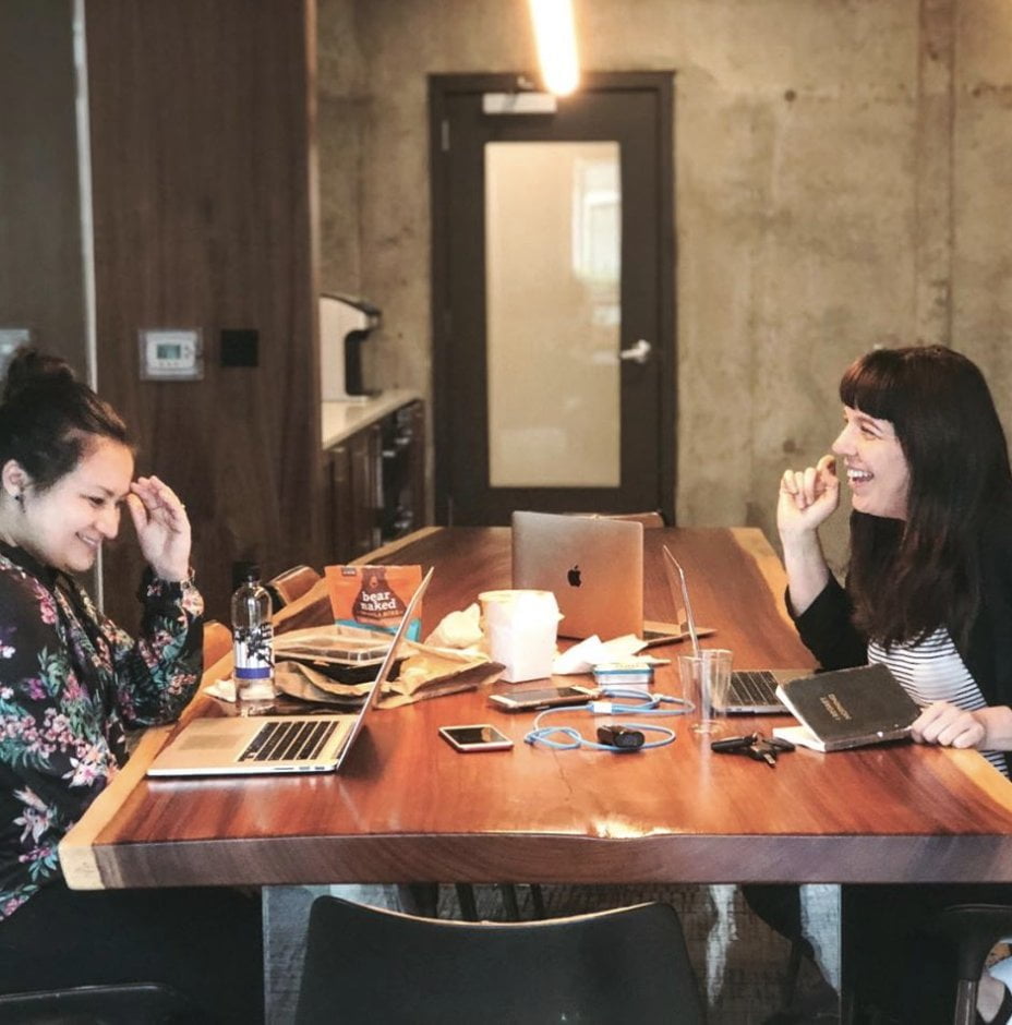 marguerite and alyssa sitting at a wooden table with laptops and notes all around