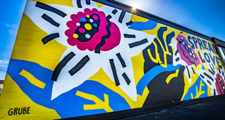 A photo of a mural on a sunny day in Sumner, Washington. The mural is bright yellow and blue and features a hand and daffodils.