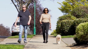 A photo of two people living in gig harbor wa walking a small dog on a sidewalk.