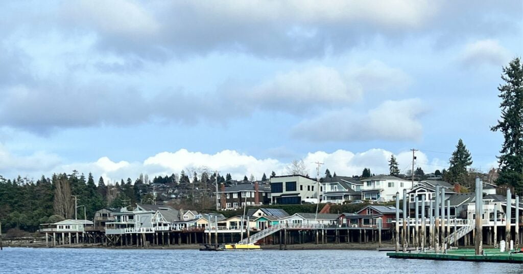 A photo of the Titlow Beach waterfront neighborhood of Tacoma Washington taken from the water. A row of houses on piers perch above the waters of the puget sound.