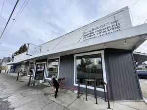 Exterior of Delightful Market in the North End of Tacoma, Washington. It's a white building with a german shepherd out front and a sign that says delightful market