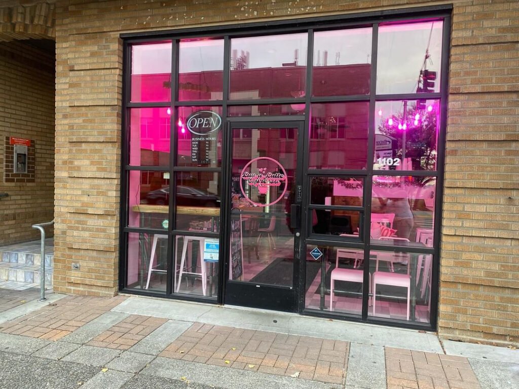 Picture of Luv a Latte Espresso exterior in Tacoma's Hilltop Neighborhood. A Brick building with large floor to ceiling windows with bright pink lighting inside. 