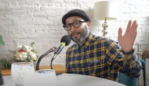 Silong Chhun wears a beanie and glasses with a plaid shirt while gesturing and speaking into a podcast mic on the Move to Tacoma Podcast.