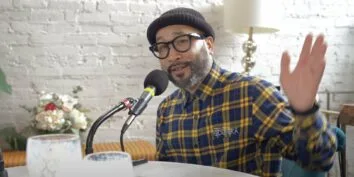 Silong Chhun wears a beanie and glasses with a plaid shirt while gesturing and speaking into a podcast mic on the Move to Tacoma Podcast.