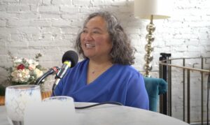 Author Tamiko Nimura sits at a table with a podcast mic in a blue shirt.