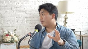 Kevin Lee owner of Third Space Coffee in Tacoma Washington talks into a podcast mic wearing a white tshirt and denim shirt