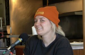 Hailey Hernandez wheres a Black Tshirt that says "Hard Rock Cafe" and an Orange Knit Hat that says "Tacoma" while smiling