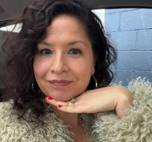 Jen Rittenhouse wears a fur coat and poses with her hand under her chin.