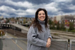 tacoma relocation expert marguerite martin stands on the glass bridge in tacoma wa wearing a warm grey sweater and smiling at the camera