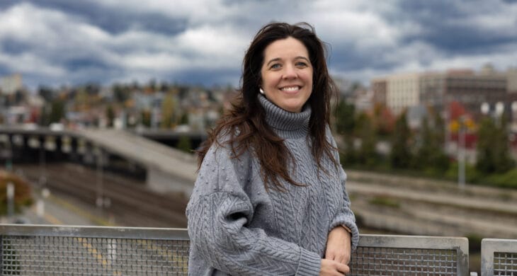 tacoma relocation expert marguerite martin stands on the glass bridge in tacoma wa wearing a warm grey sweater and smiling at the camera