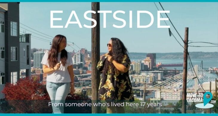 Two tacoma real estate agents with long hair walking up McKinley Hill talking to each other with Downtown Tacoma in the background with the words, "Eastside: From someone whose lived here 17 years"